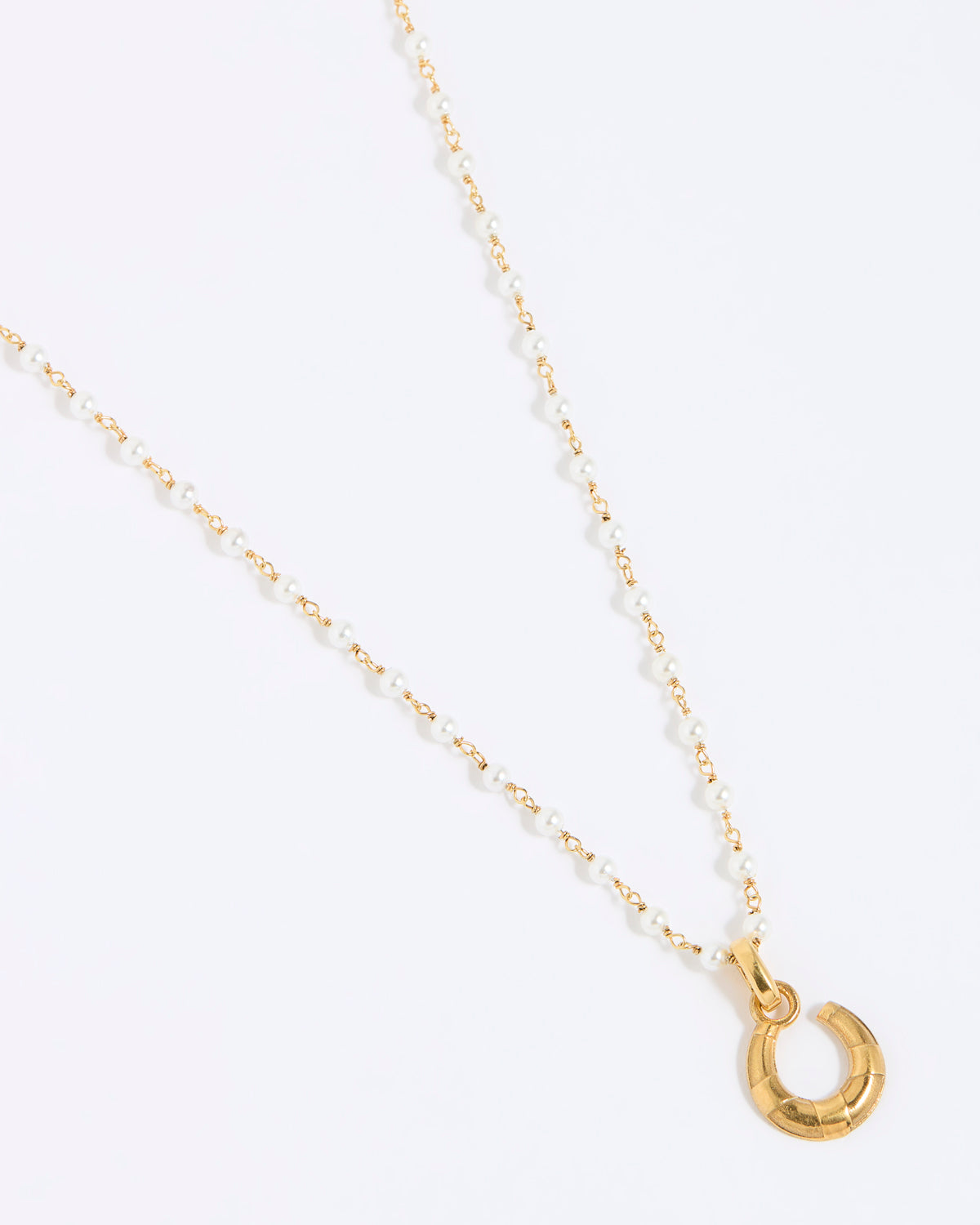 Gold coloured and pearl necklace with a small horseshoe pendant on a white background