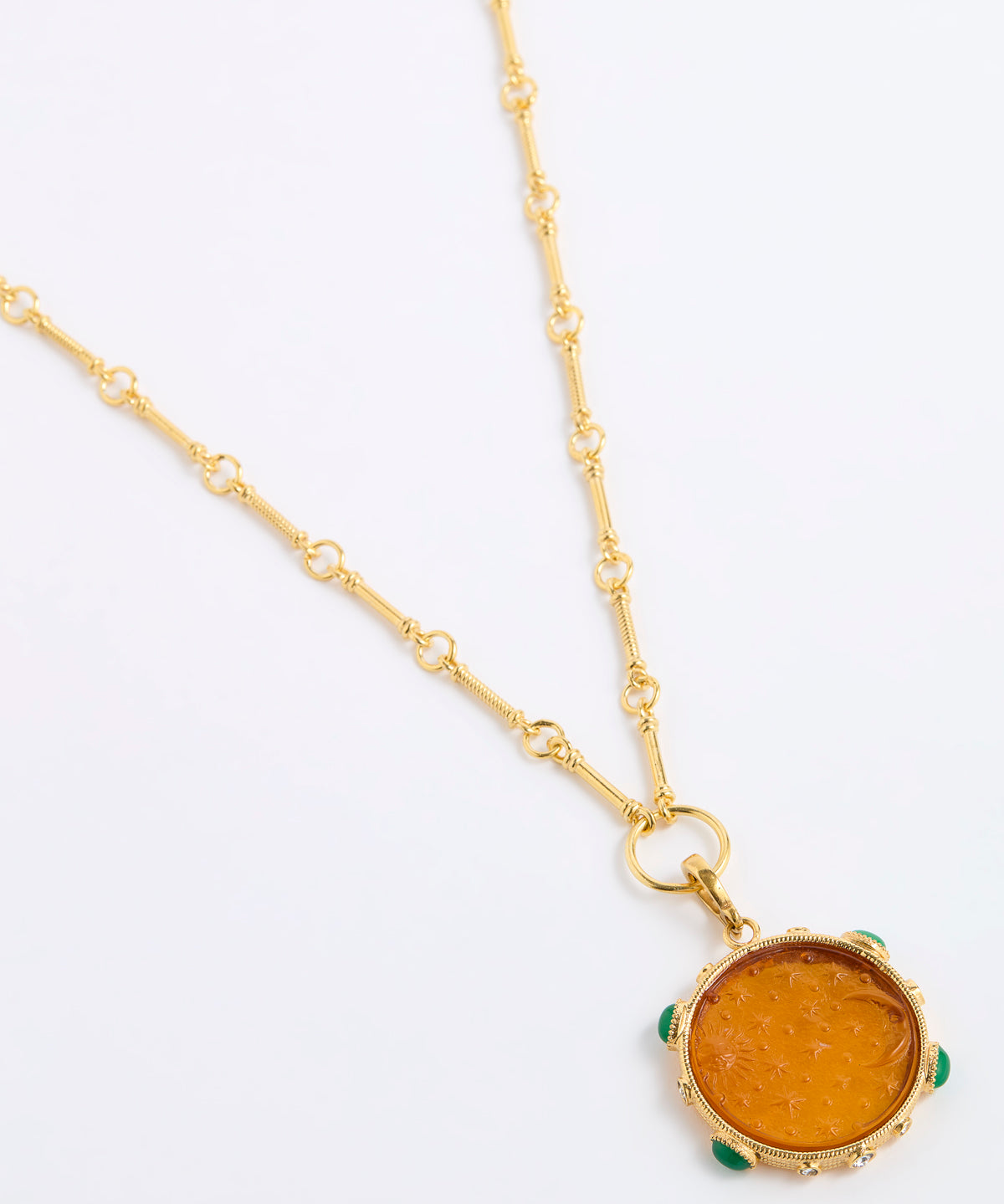 A gold chain necklace featuring a round amber-colored pendant with small green stone accents around its edge, displayed on a clean white background.