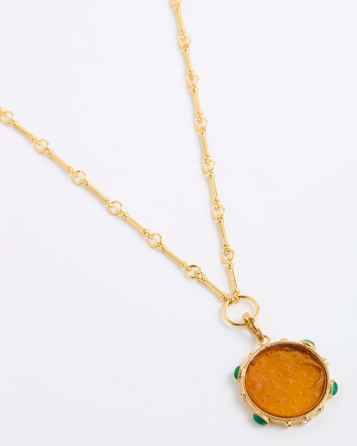 A gold chain necklace featuring a round amber-colored pendant with small green stone accents around its edge, displayed on a clean white background.