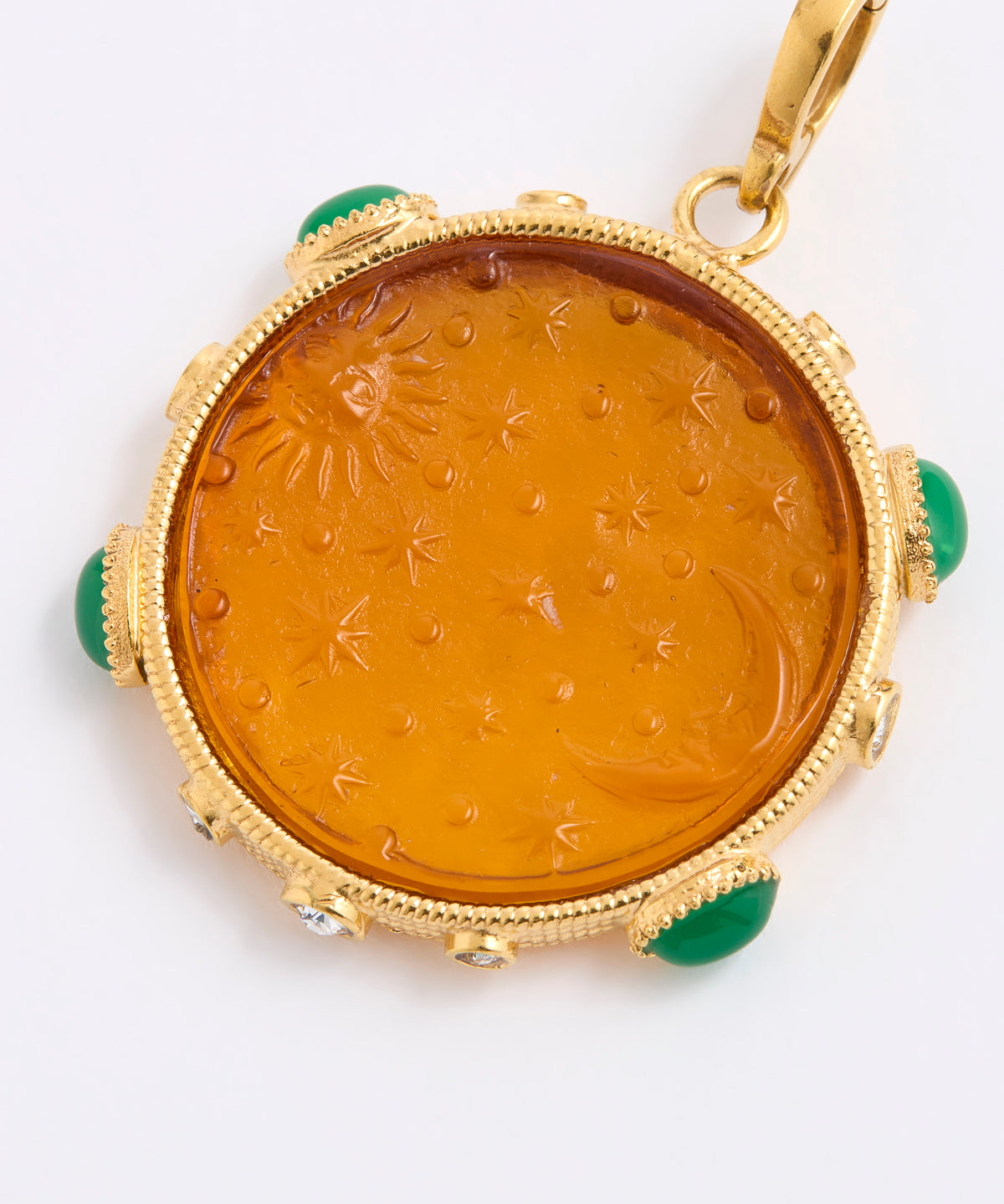 A round amber pendant with a carved sun and moon motif, set in a gold frame with green stone accents, shown on a white background.
