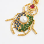 product shot of scarab beetle charm encrusted with red, bue and green crystals and one pearl on the back close up