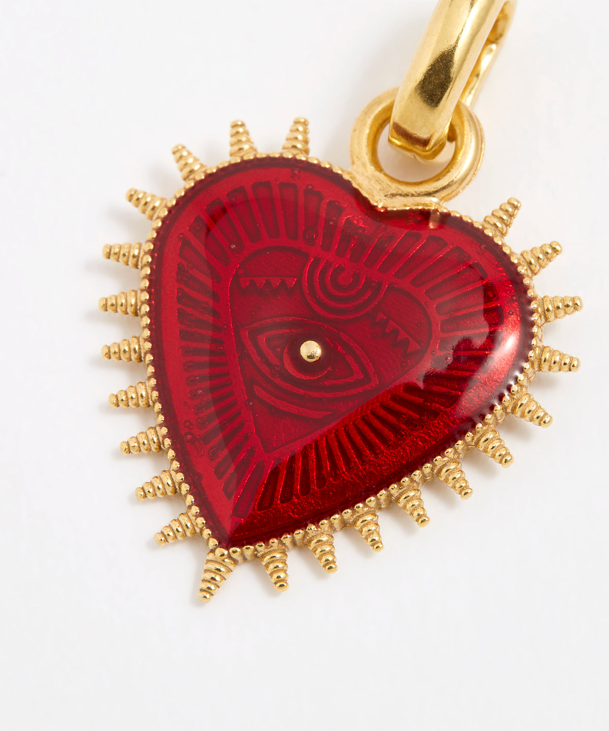 Close up product shot of a heart-shaped pendant featuring a deep, glossy red patterned enamel centre. The heart is surrounded by a border of gold spikes that extend outward from the edges.