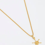 Product shot of gold ships wheel charm hung from a rope chain on a white background