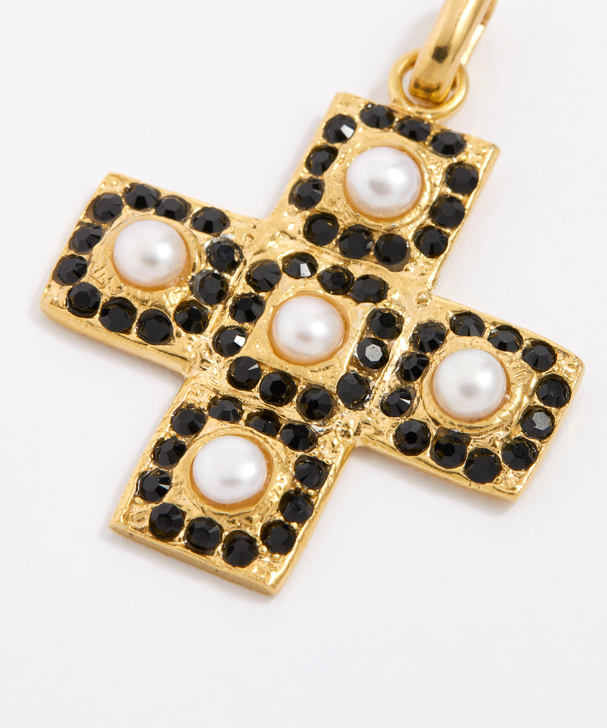 Close up overhead image of the gold textured cross-shaped pendant embellished with alternating baroque pearls and black crystals on a white background.