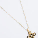 Product image of a gold textured cross-shaped pendant embellished with alternating baroque pearls and black crystals hung from a Soru pearl charm chain on a white background.