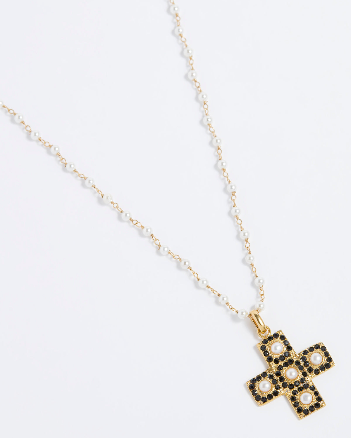 Product image of a gold textured cross-shaped pendant embellished with alternating baroque pearls and black crystals hung from a Soru pearl charm chain on a white background.
