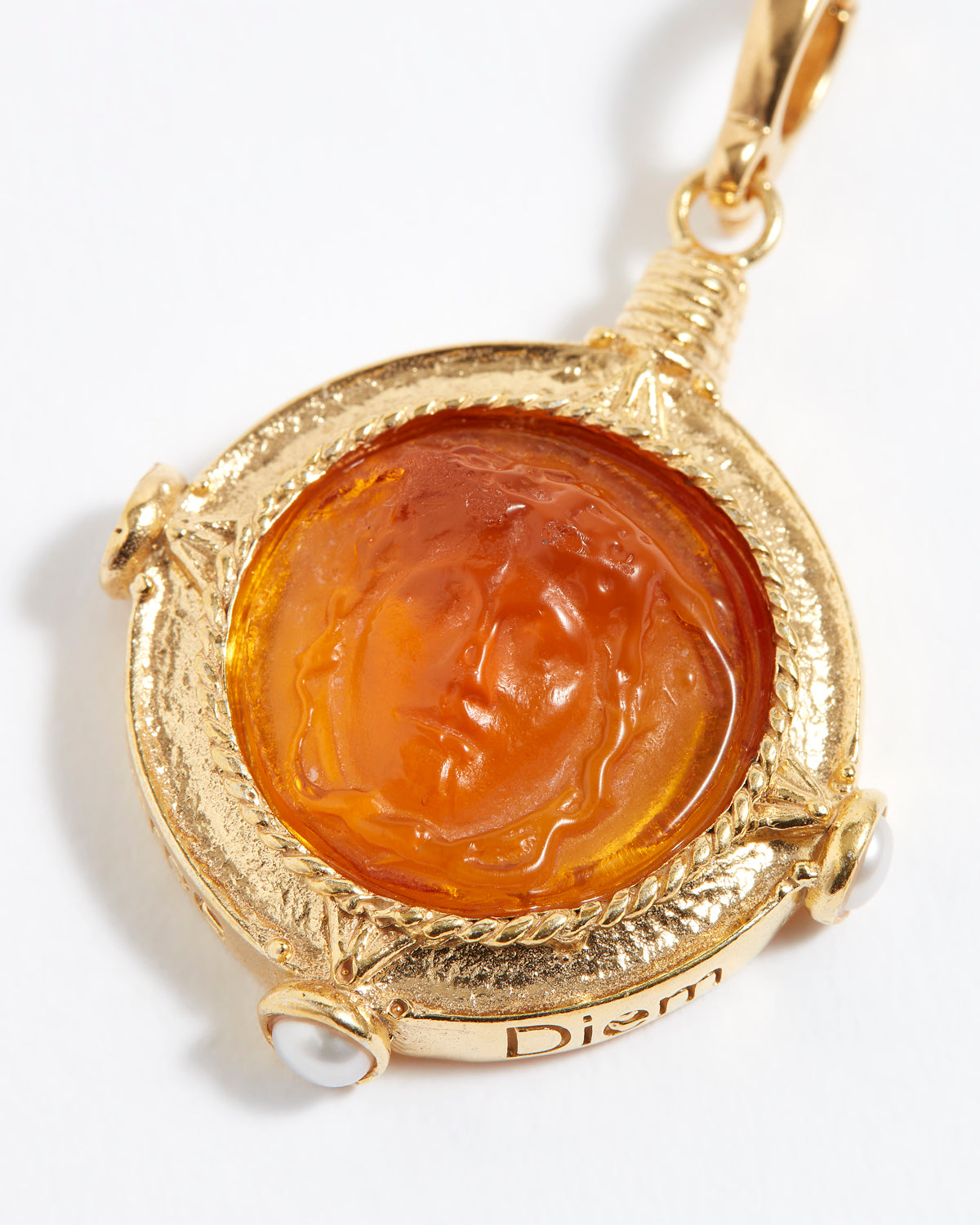Gold pendant with a central topaz-colored stone on a white background