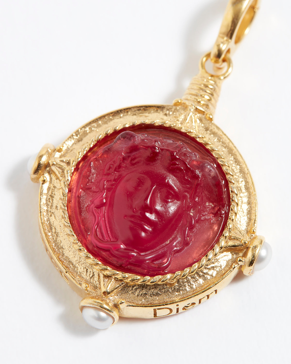 Gold pendant with a red gemstone featuring an engraved face on a white background