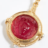 Gold pendant with a red gemstone featuring an engraved face on a white background