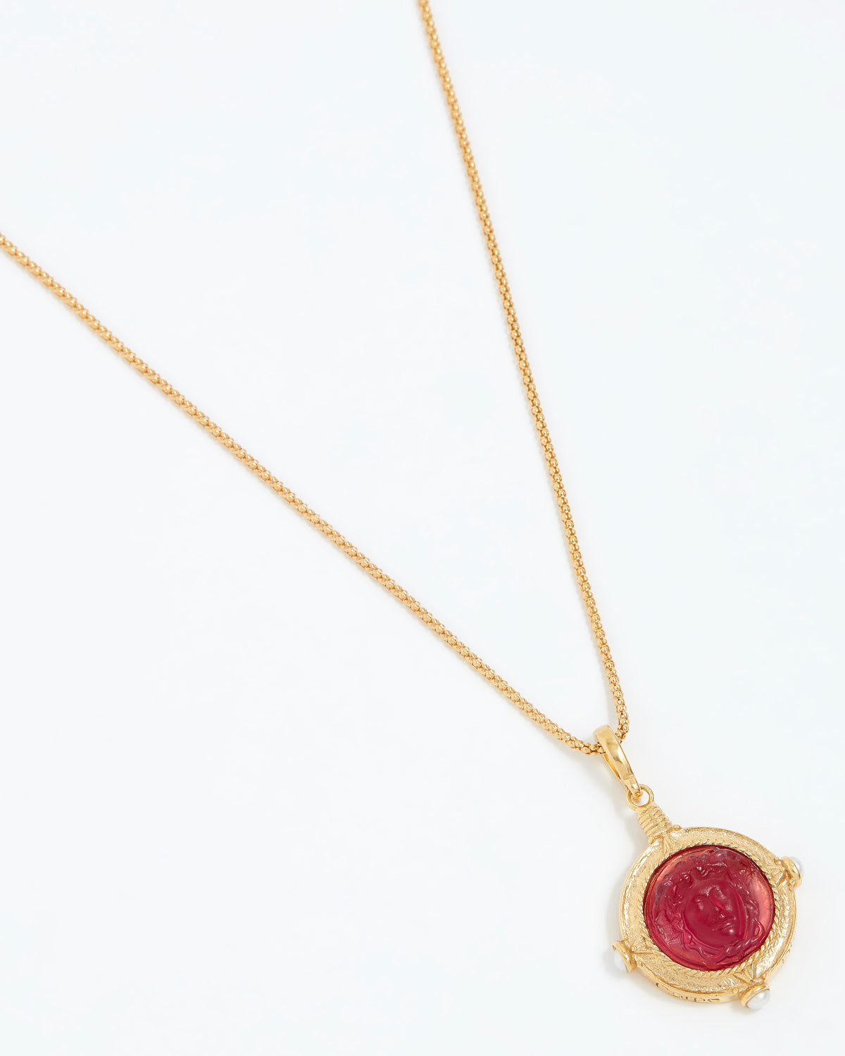 Gold necklace with a red gemstone pendant on a white background