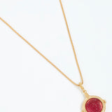 Gold necklace with a red gemstone pendant on a white background
