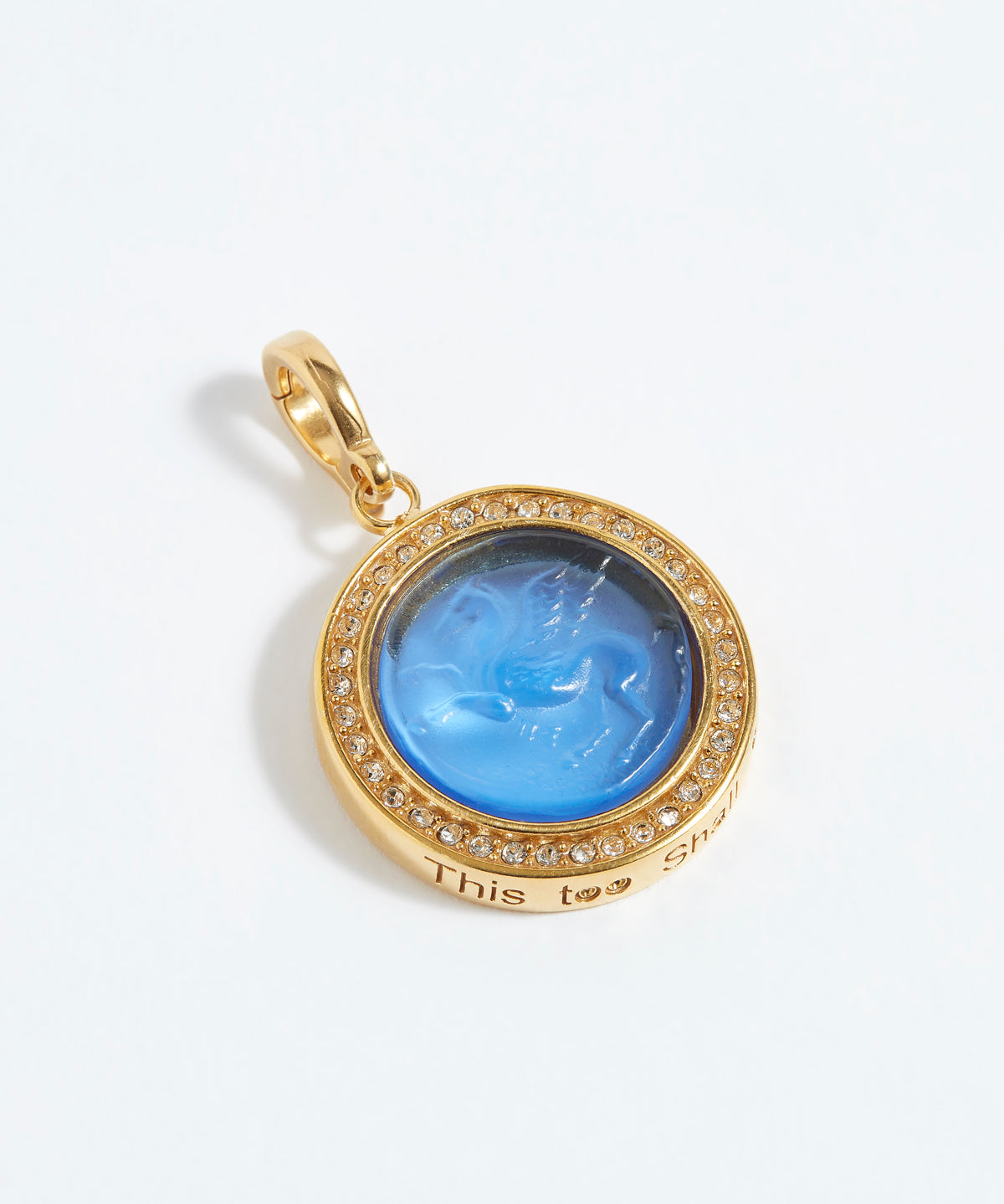 Gold pendant with blue stone and engraved text "this too shall pass" on a white background