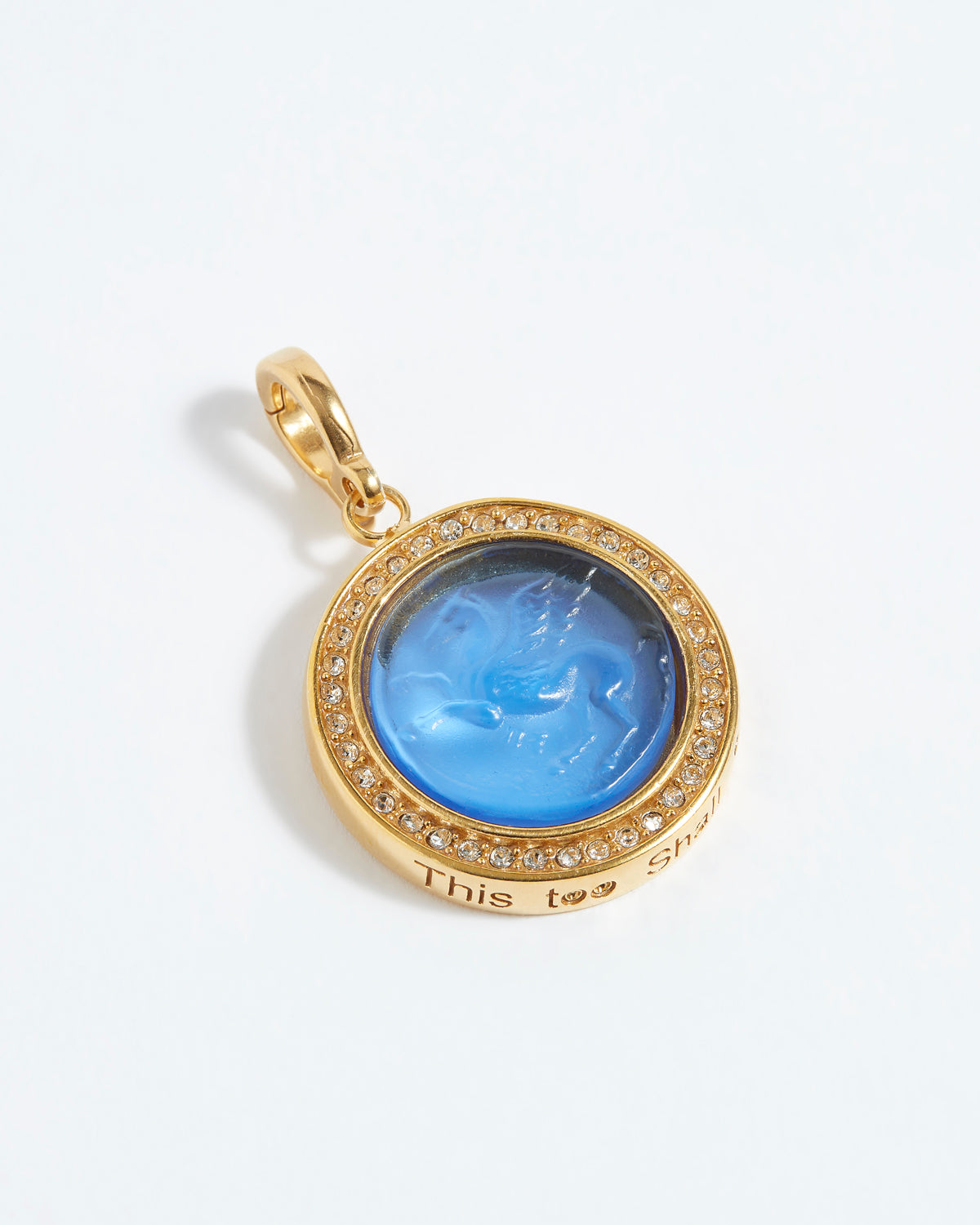 Gold pendant with blue stone and engraved text "this too shall pass" on a white background