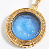 Gold pendant with blue central stone and "this too shall pass" engraving on a white background