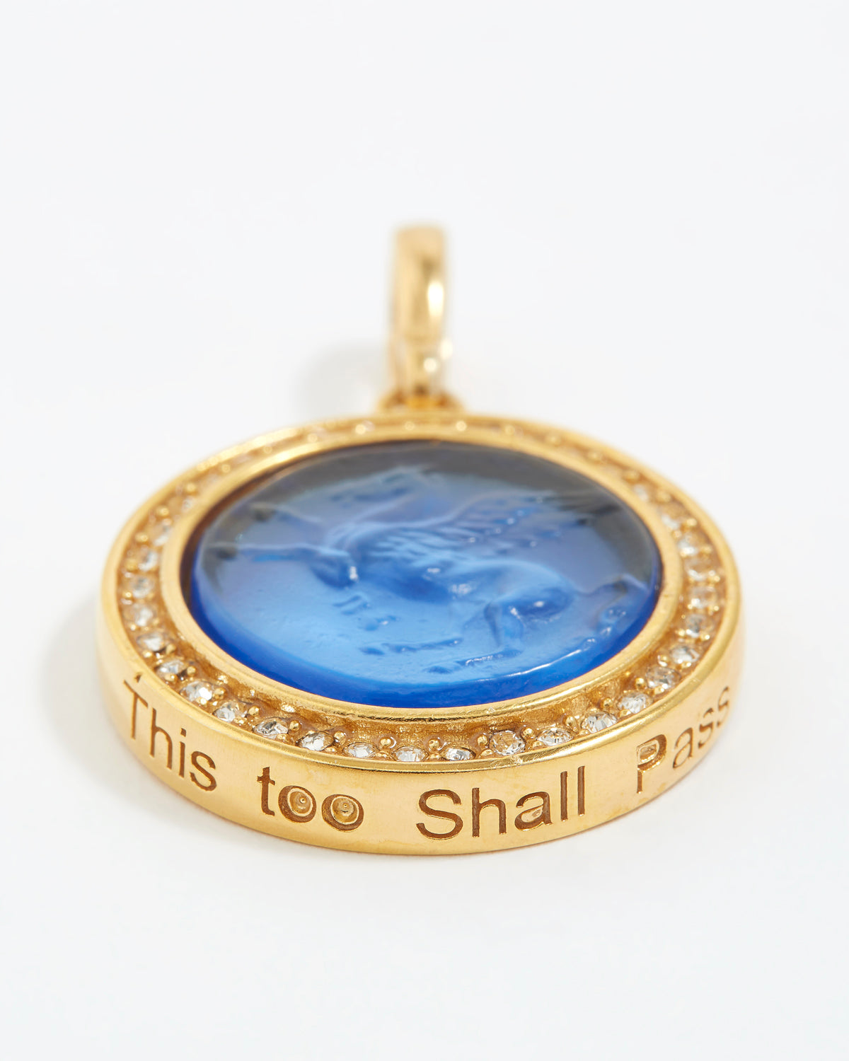 Gold pendant with blue center and engraved text "this too shall pass" on a white background