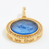 Gold pendant with blue center and engraved text "this too shall pass" on a white background