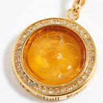 Gold pendant with a yellow center and embedded crystals on a white background