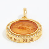 Gold pendant with engraved text "this too shall pass" on a white background