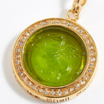 Gold pendant with green gemstone and engraved design "this too shall pass" on a white background