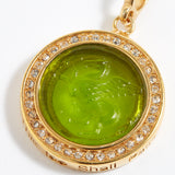 Gold pendant with green gemstone and engraved design "this too shall pass" on a white background