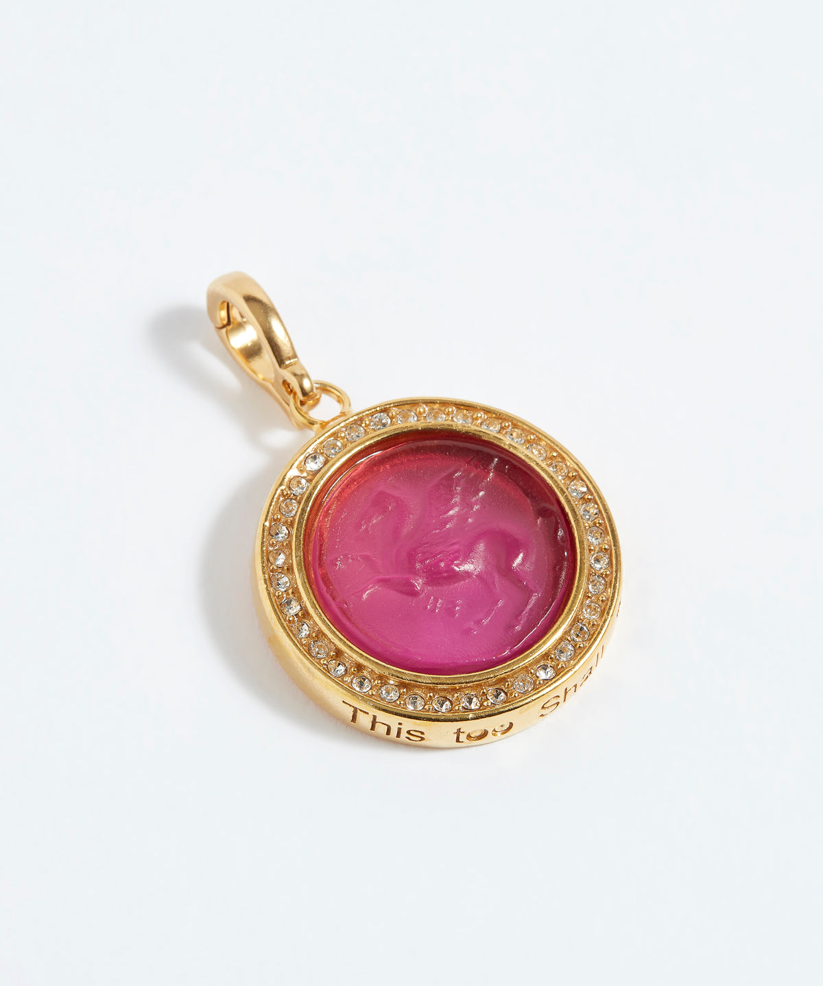 Gold pendant with pink gemstone and engraved text "this too shall pass" on a white background