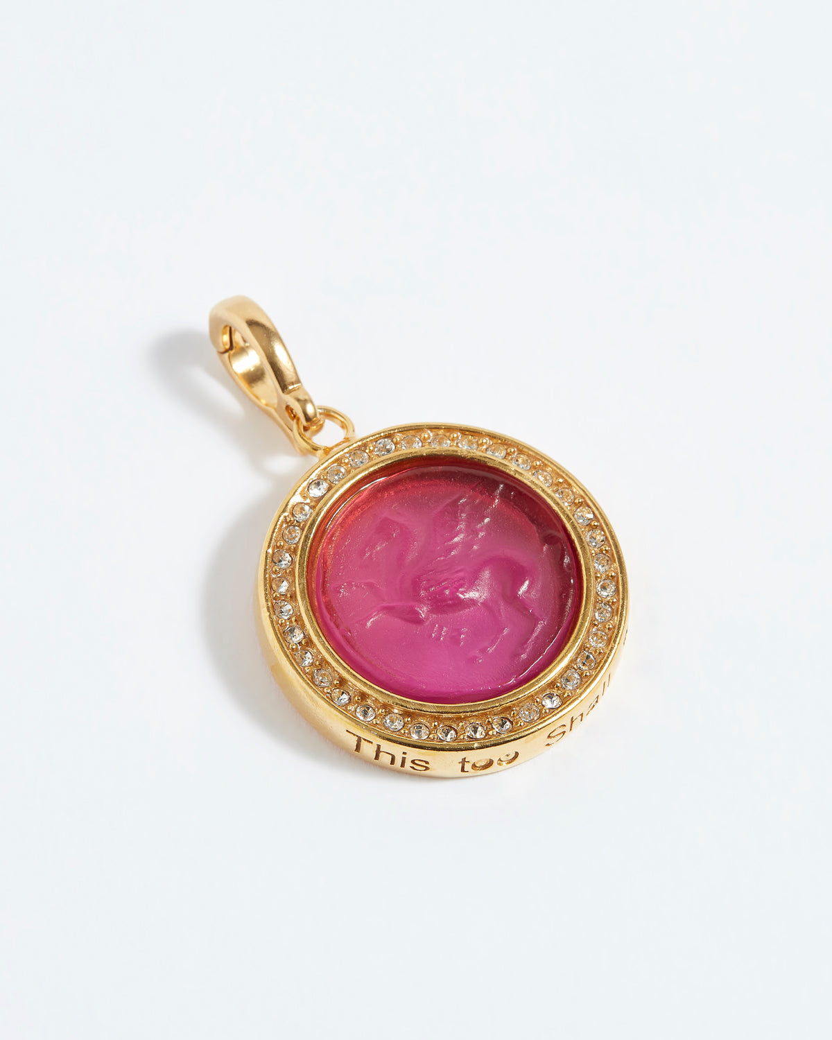 Gold pendant with pink gemstone and engraved text "this too shall pass" on a white background