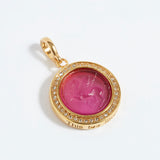 Gold pendant with pink gemstone and engraved text "this too shall pass" on a white background