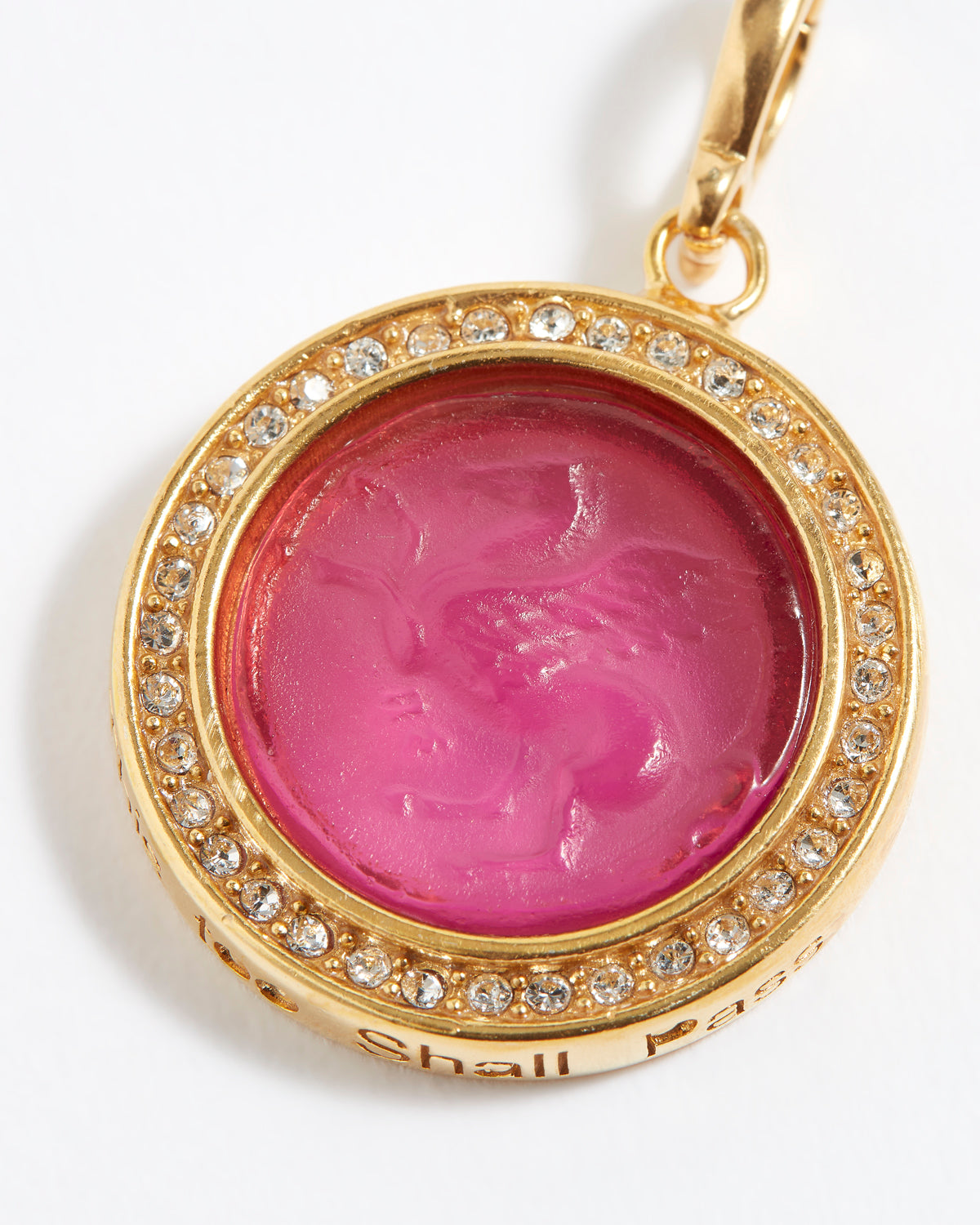 Gold pendant with pink gemstone and engraved text "this too shall pass"  on a white background