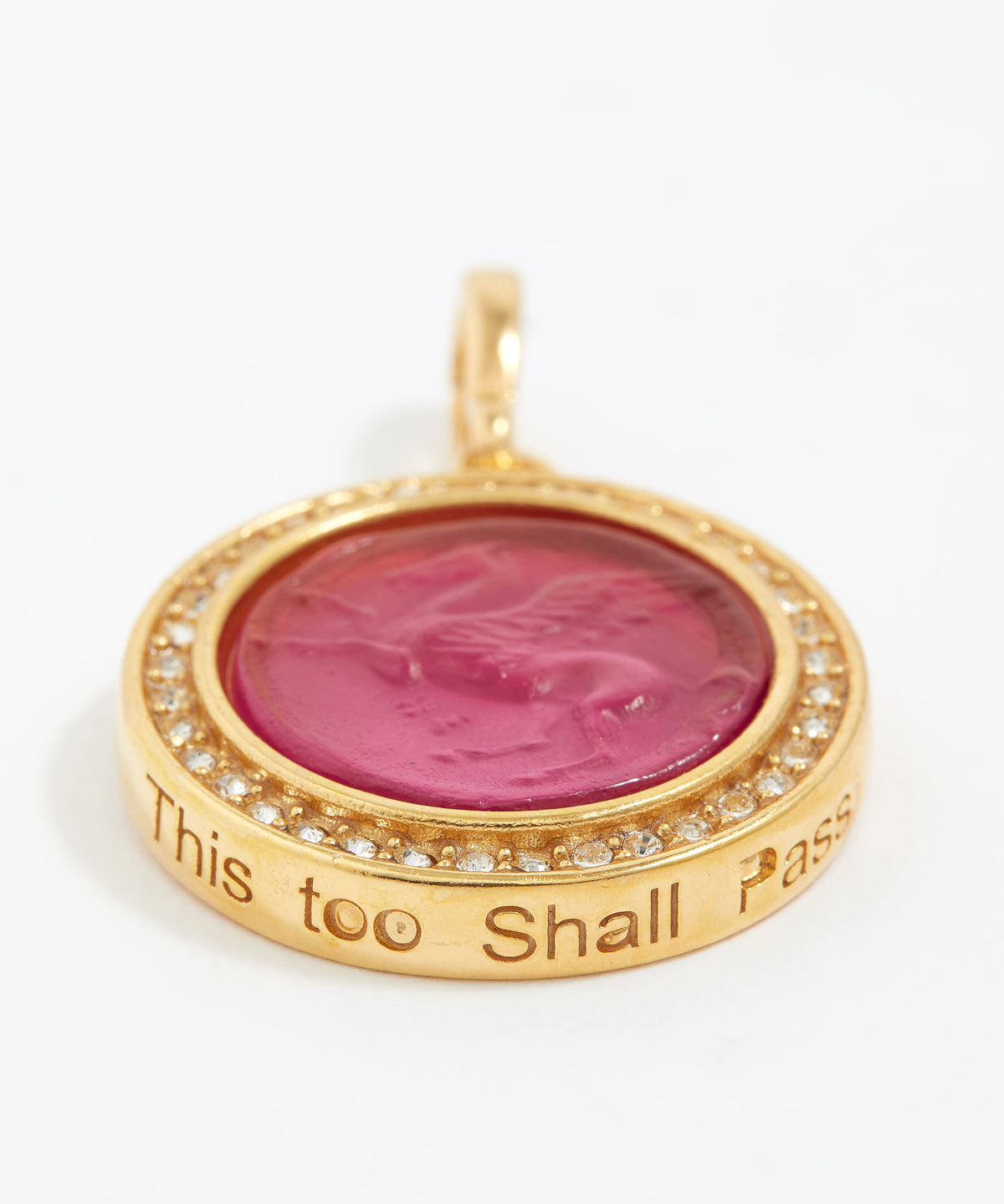 Gold pendant with pink center and engraved text "this too shall pass" on a white background