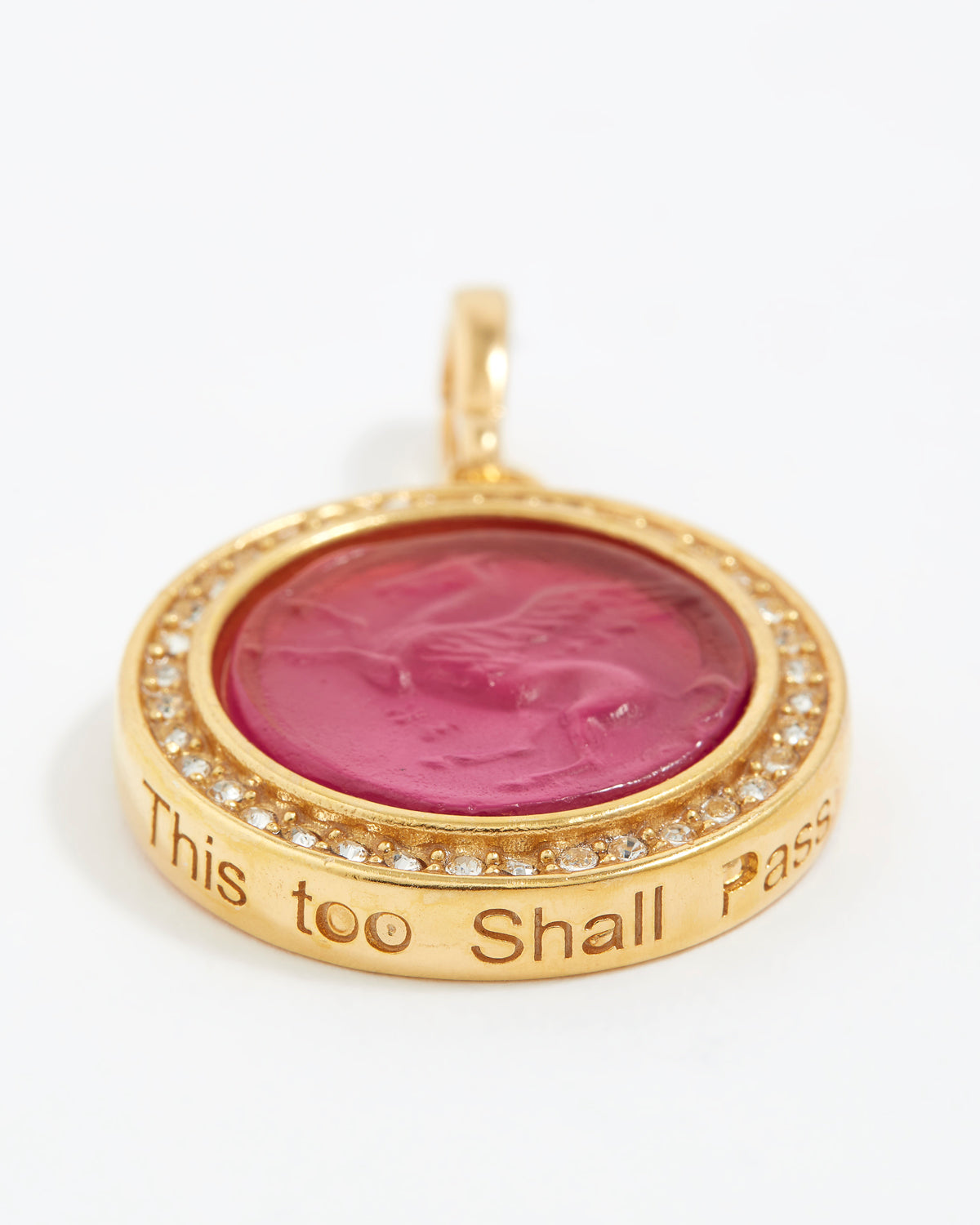 Gold pendant with pink center and engraved text "this too shall pass" on a white background