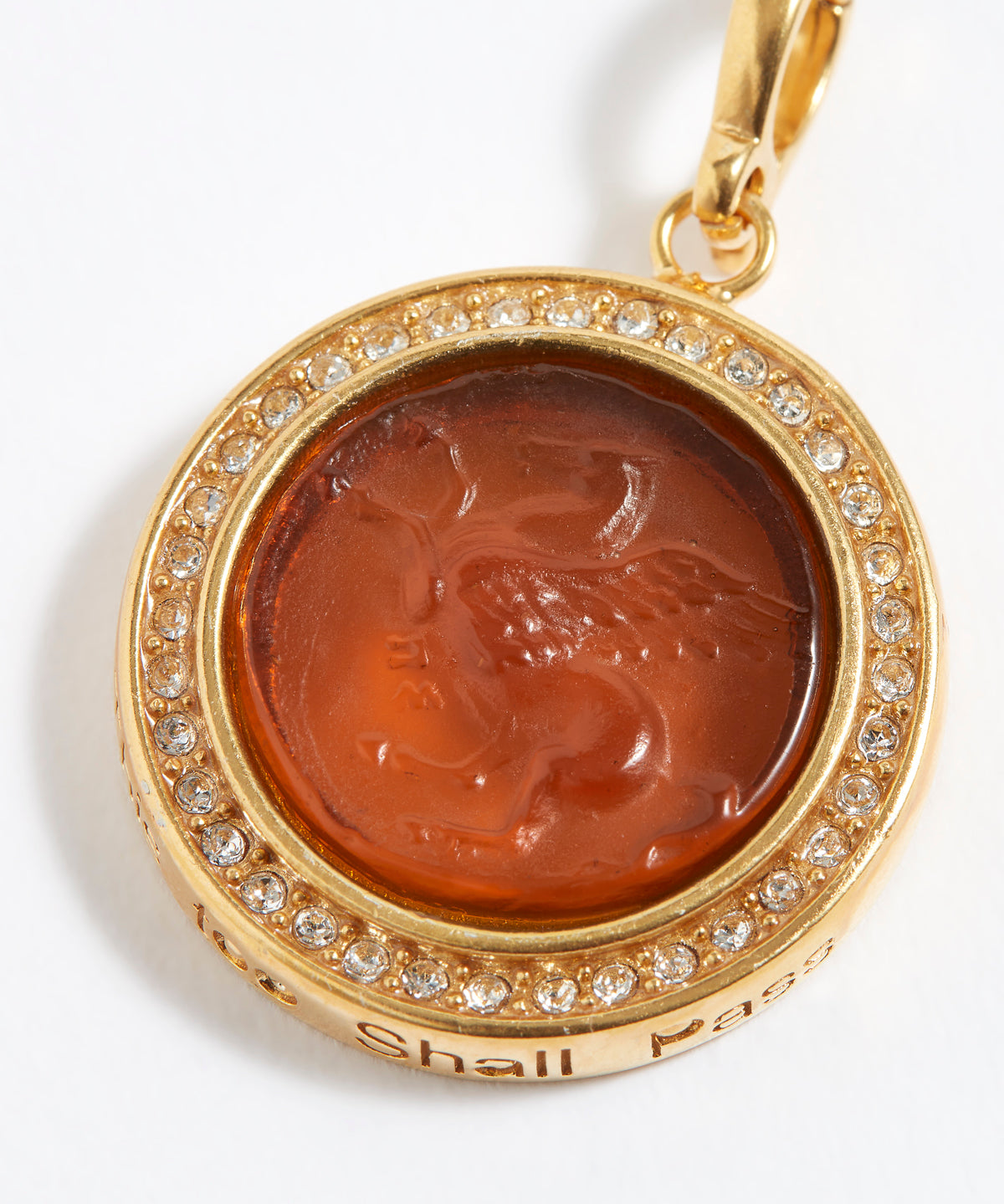 Gold pendant with a raised emblem and gemstones on a white background