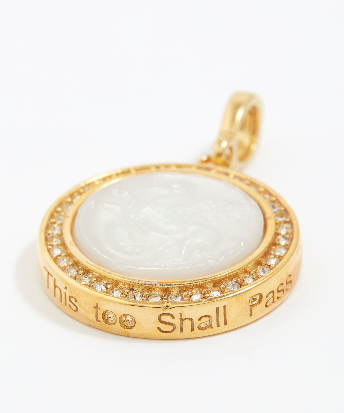 Gold pendant with white stone and engraved text "this too shall pass" on a white background