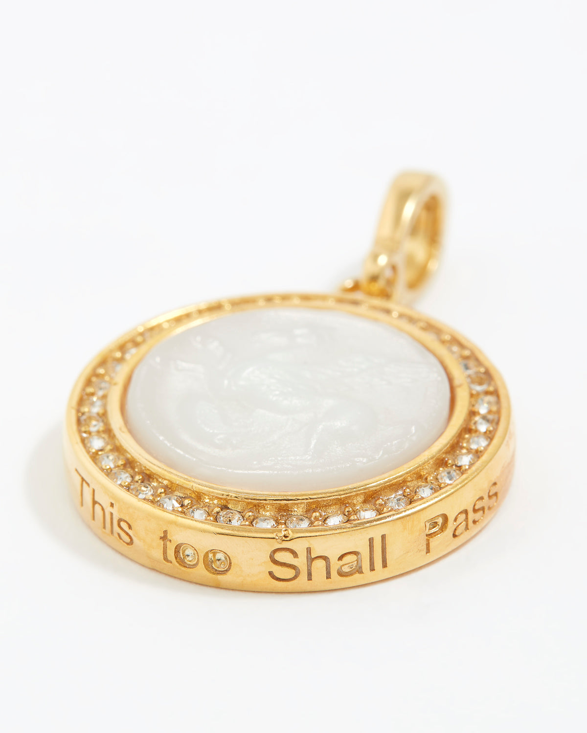 Gold pendant with white stone and engraved text "this too shall pass" on a white background