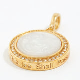 Gold pendant with white stone and engraved text "this too shall pass" on a white background