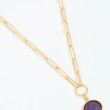 Gold necklace with a purple pendant on a white background