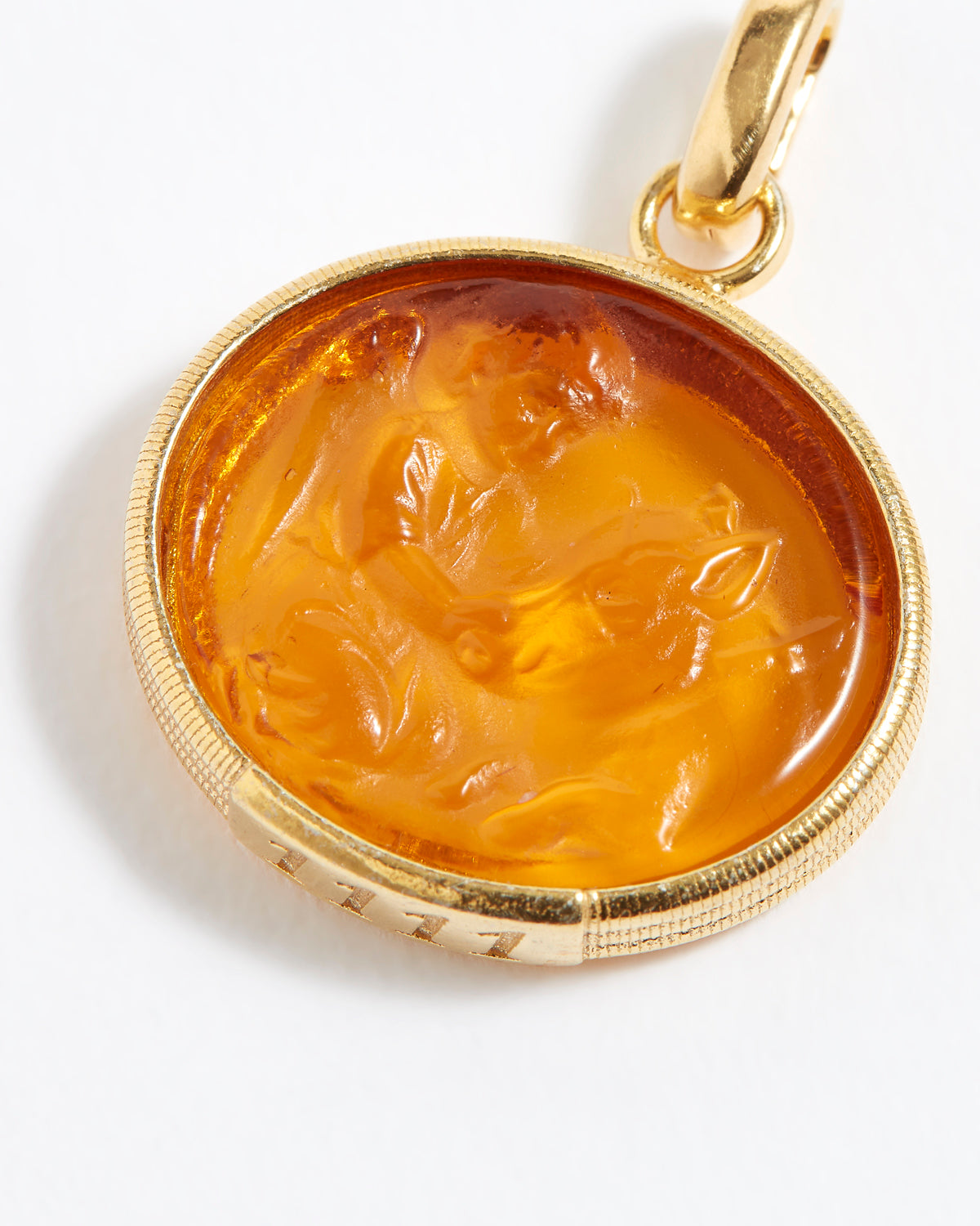 Gold pendant with a carved topaz stone on a white background