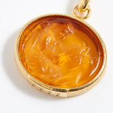 Gold pendant with a carved topaz stone on a white background