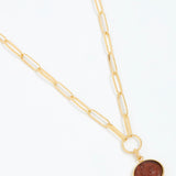 Gold necklace with a round topaz pendant on a white background