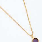 Gold necklace with a purple pendant on a white background