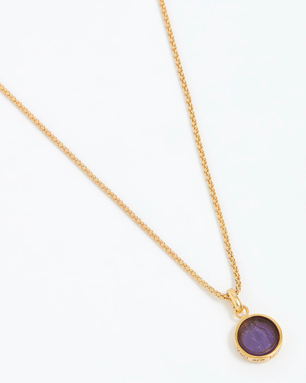 Gold necklace with a purple pendant on a white background