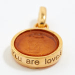 Gold pendant with brown center and 'You are loved' engraving on a white background