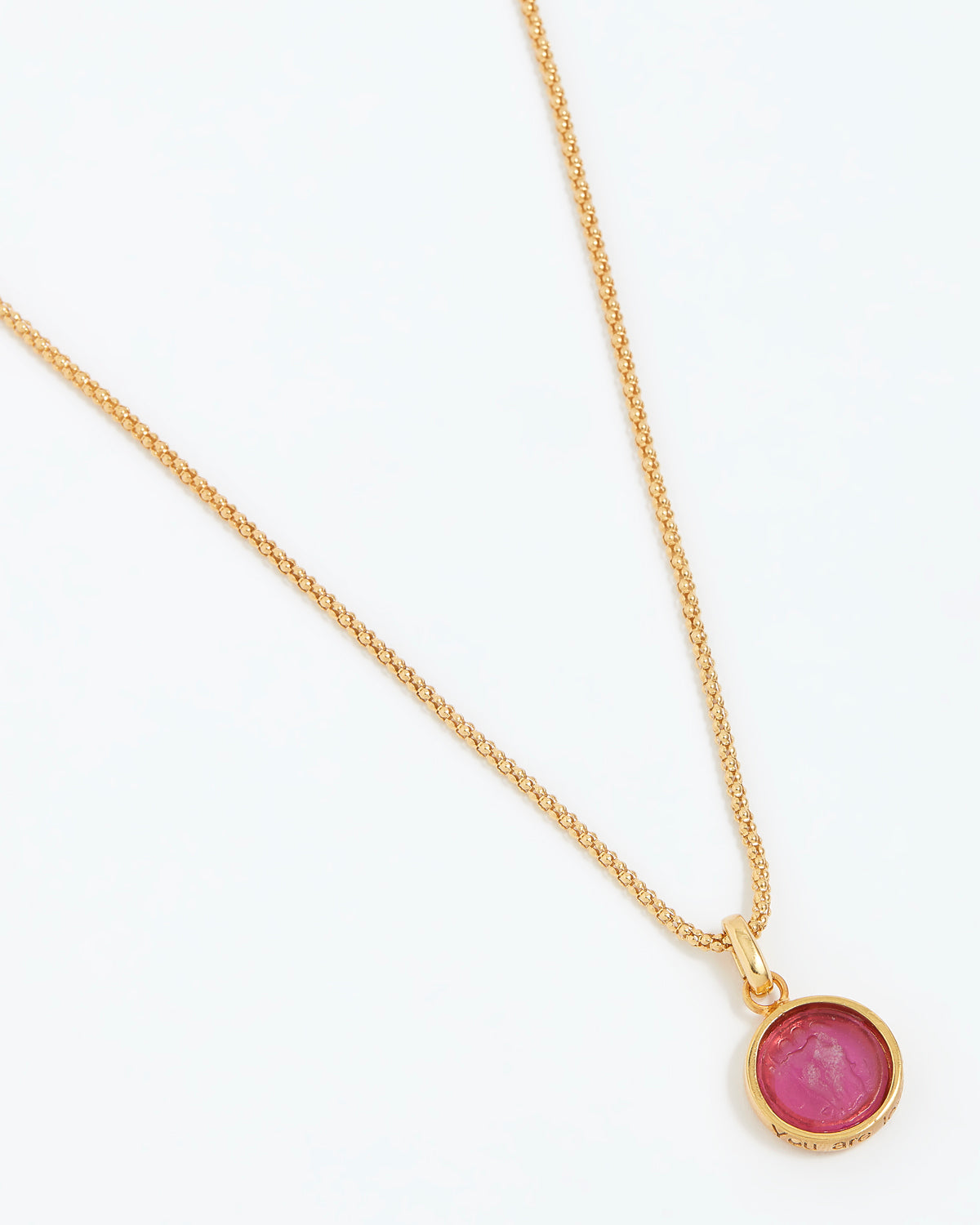 Gold necklace with a pink gemstone pendant on a white background