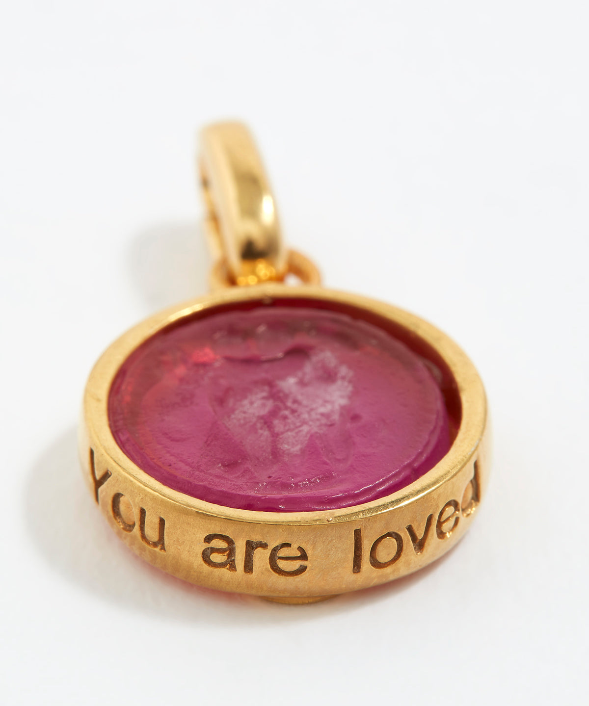 Gold pendant with pink stone and engraved text  “You Are Loved” on a white background