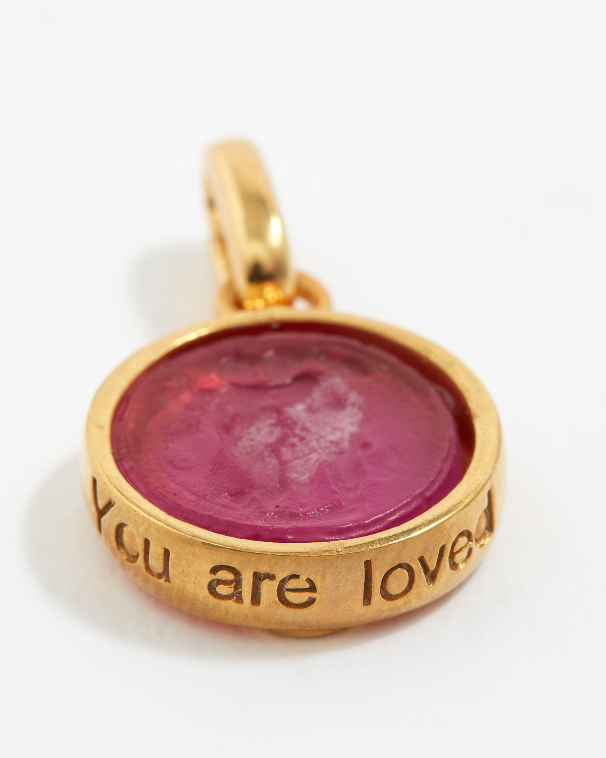 Gold pendant with pink stone and engraved text  “You Are Loved” on a white background