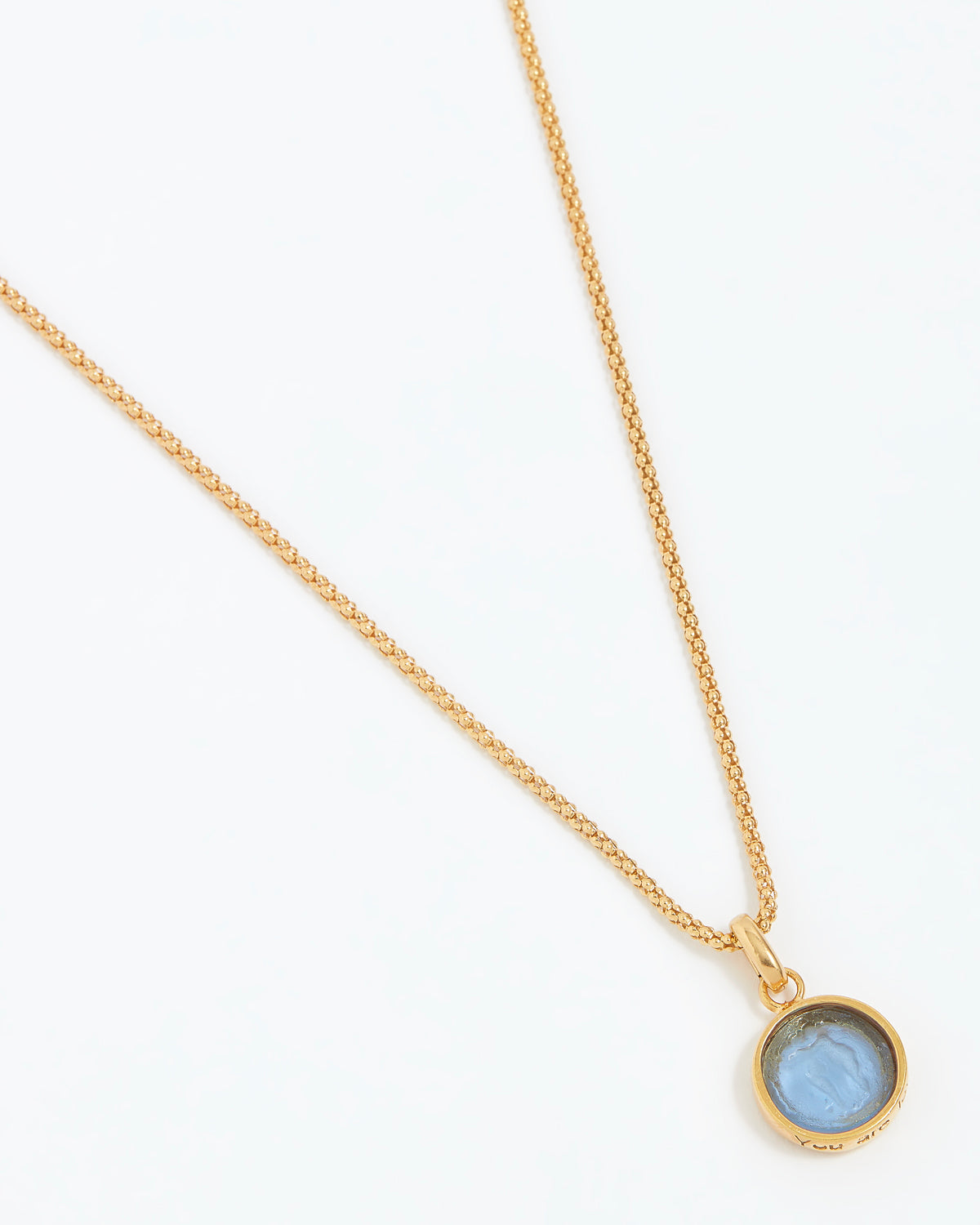 Gold necklace with a blue gemstone pendant on a white background
