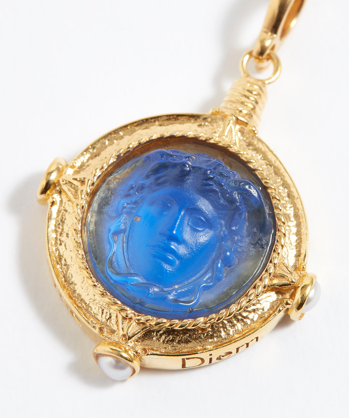 Gold pendant with blue stone featuring a face design on a white background