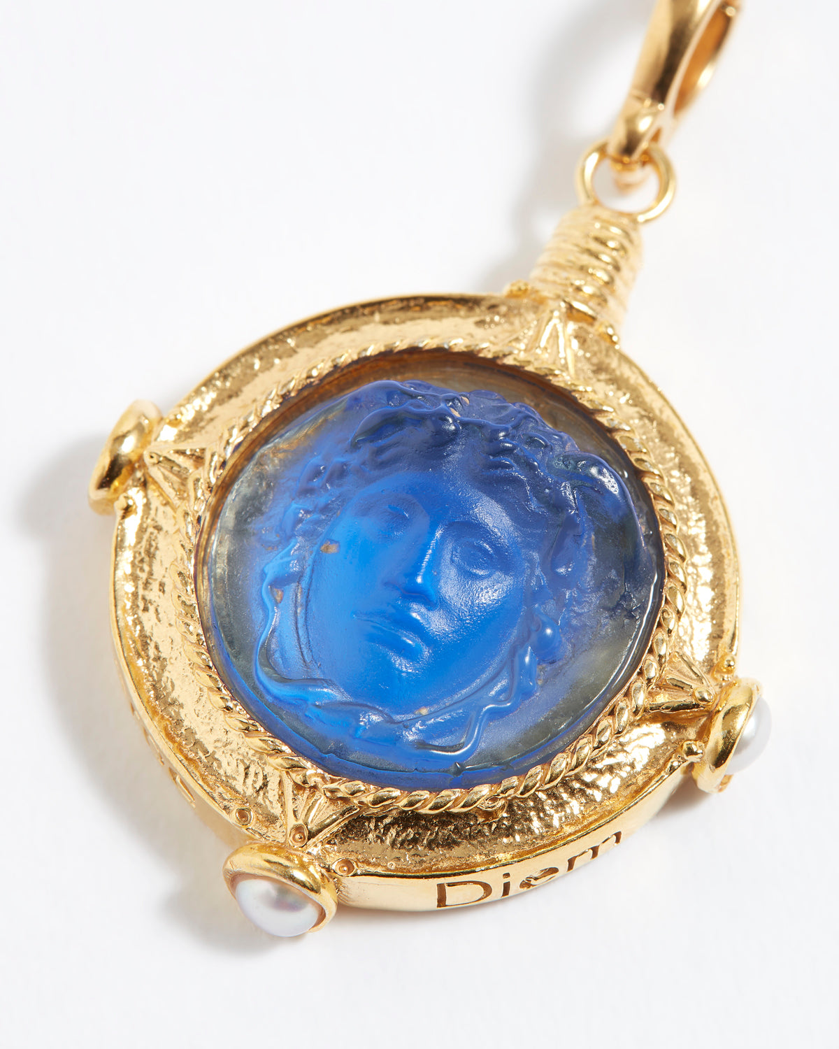 Gold pendant with blue stone featuring a face design on a white background