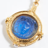 Gold pendant with blue stone featuring a face design on a white background