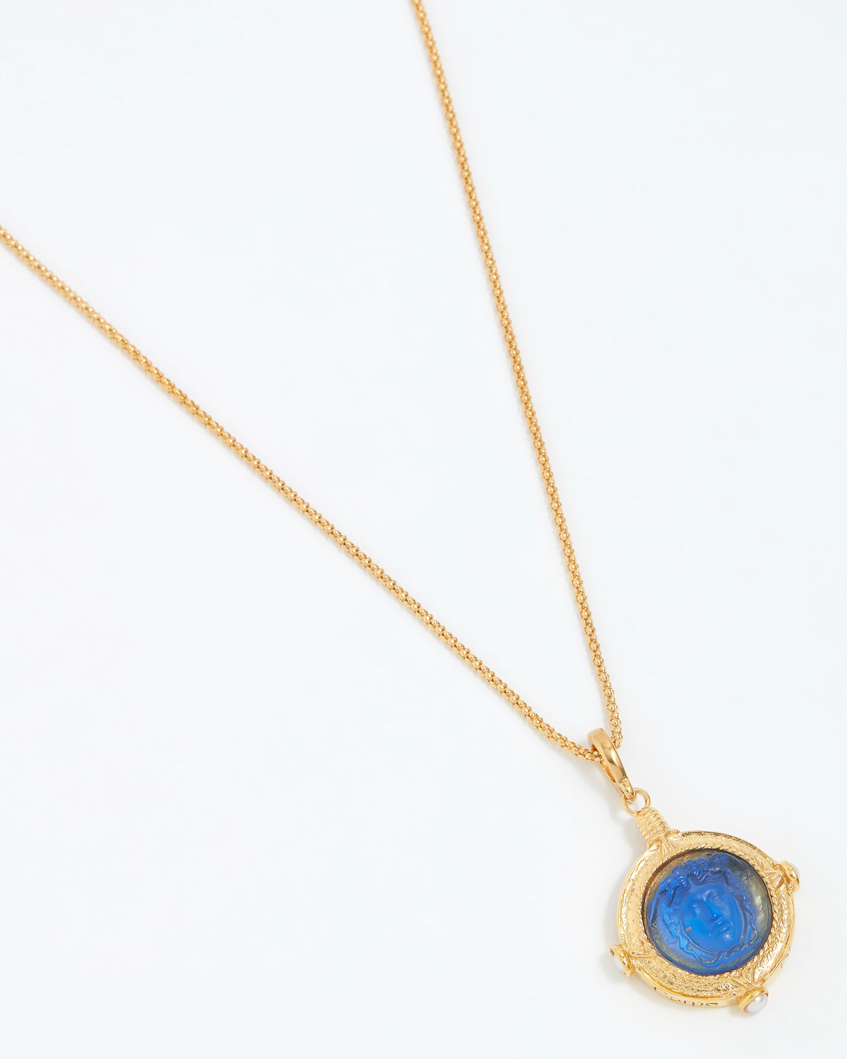 Gold necklace with a blue gemstone pendant on a white background