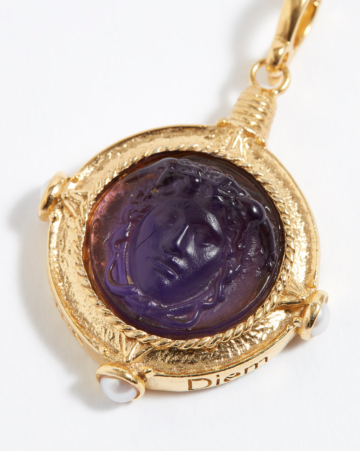 Gold pendant with purple stone featuring a face design on a white background